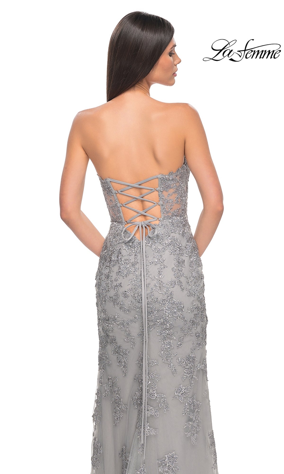 A woman stands facing away, wearing the La Femme Sheer-Corset Long Prom Dress 32013 with a strapless sweetheart neckline, lace-up back, and floral embroidery. The